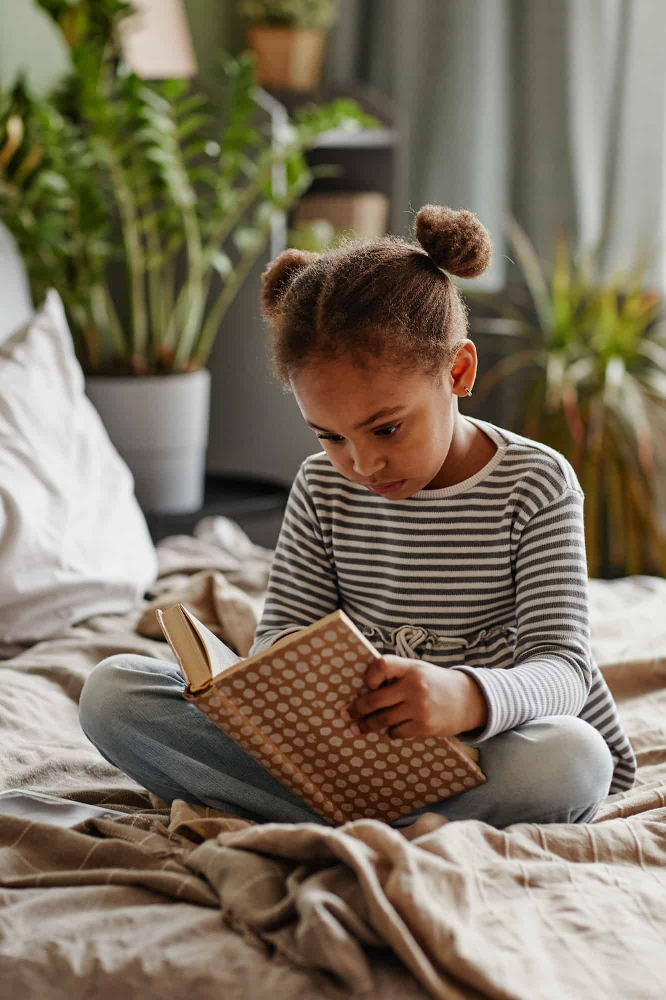 Cute African American Girl Reading Book on Bed